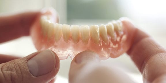 Hands holding the lower arch of a set of dentures